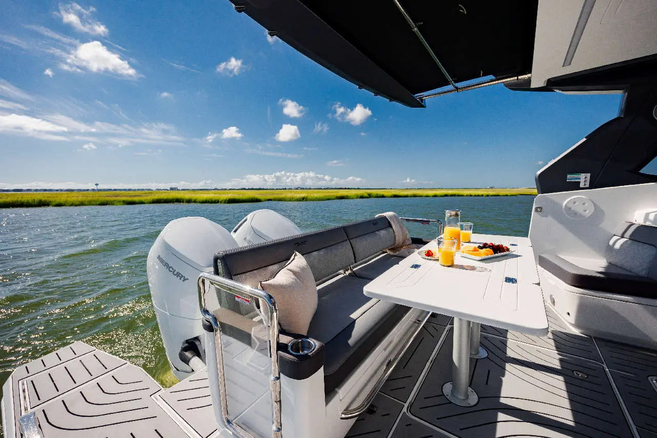 Luxury boat deck with sofa, table set for breakfast, including orange juice, fruit, and scenic water view under blue sky.