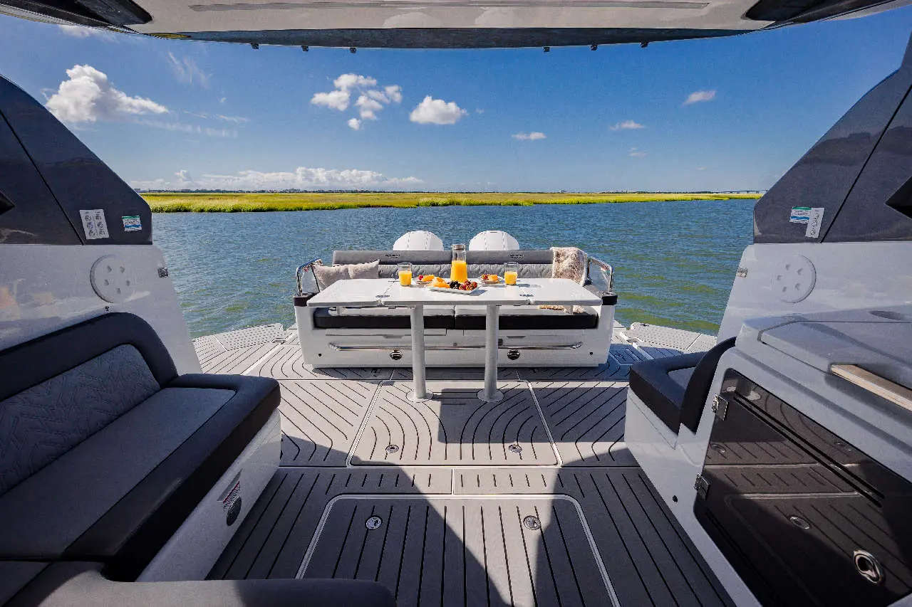 A scenic boat deck featuring a breakfast spread, with seats and a view of calm water and green shoreline under blue skies.