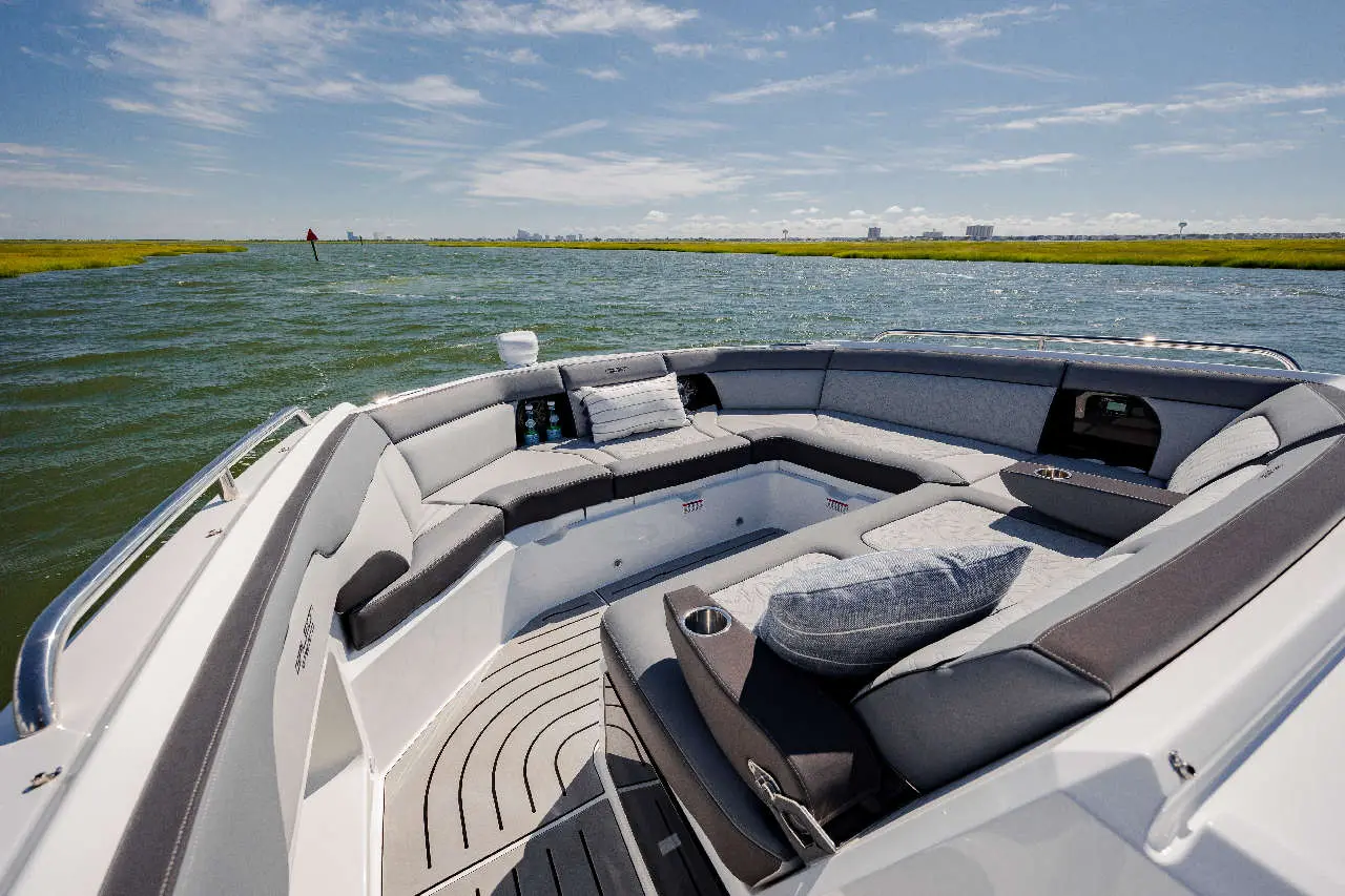 A modern boat interior features grey and black seating with a light blue cushion, surrounded by calm water and greenery.