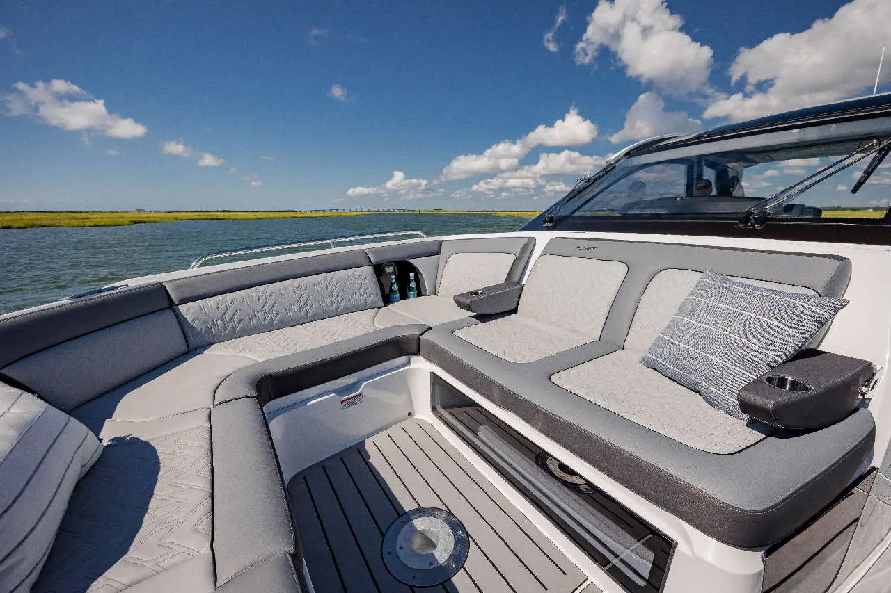 A spacious boat seating area with grey upholstery, a decorative cushion, and scenic views of water and clouds.