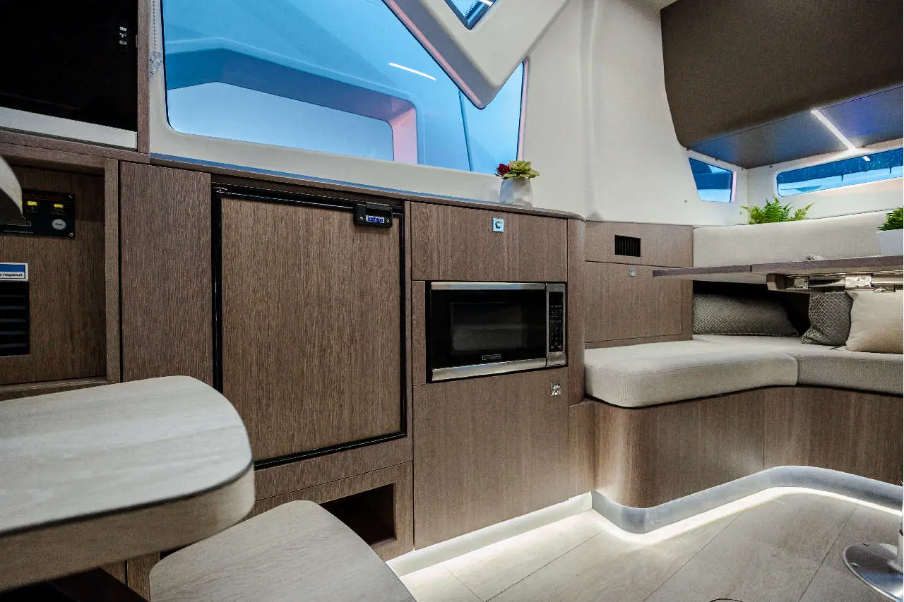 Modern yacht interior featuring a microwave, fridge, seating area, and large windows with natural light.