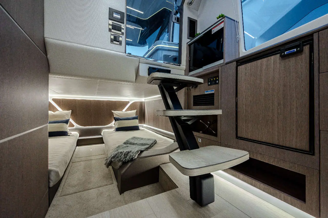 Interior view of a modern cabin with twin beds, a staircase, and built-in storage; illuminated with soft LED lights.