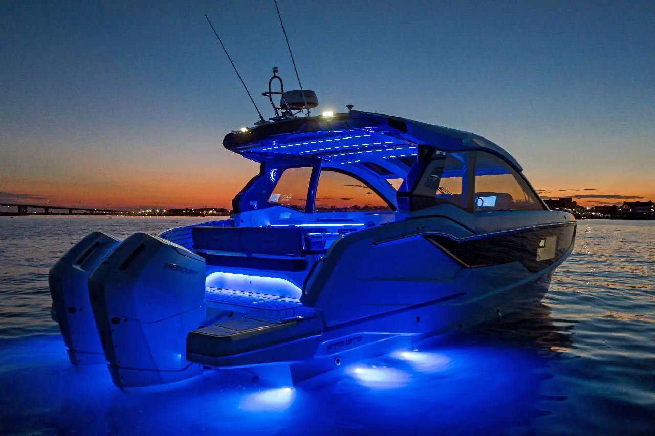 A sleek blue motorboat with illuminated features glides on calm water at sunset, showcasing modern design and luxury.