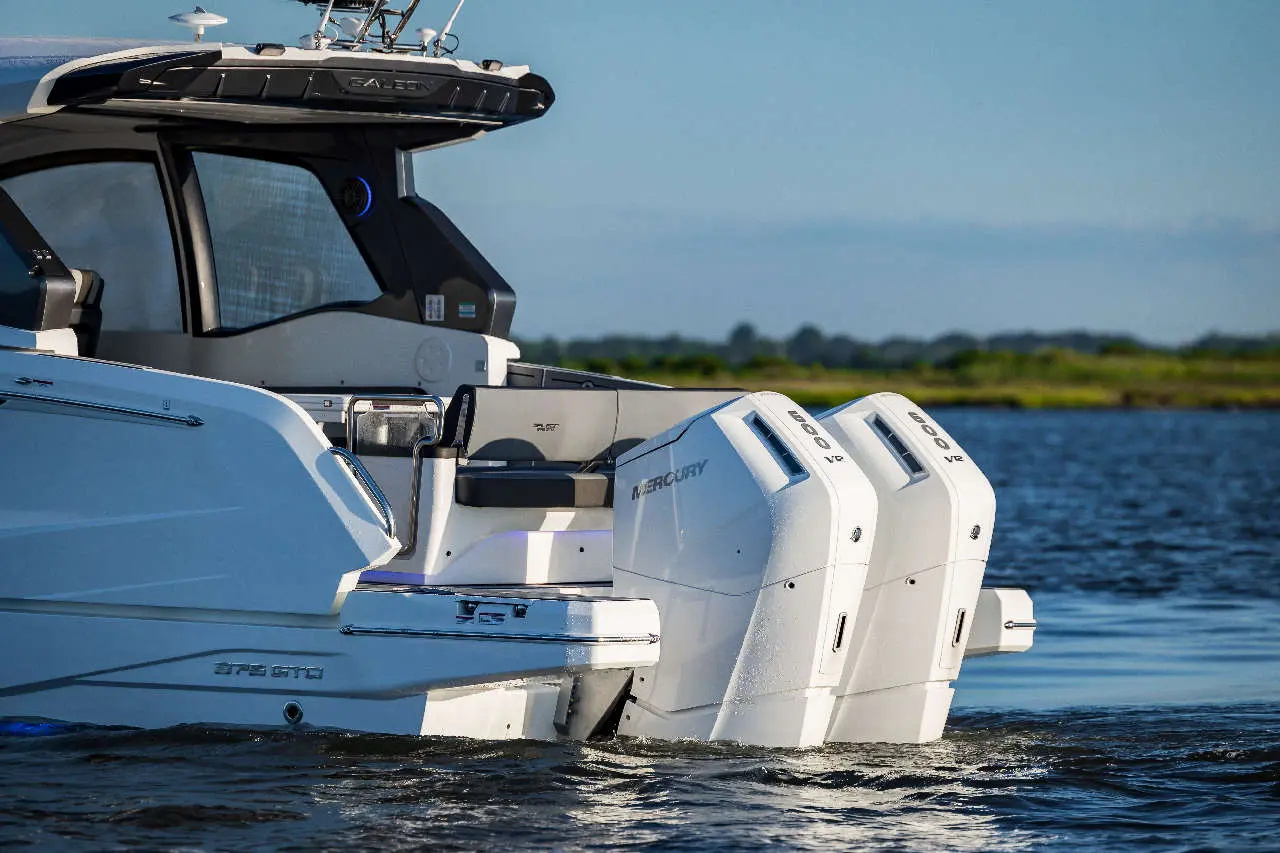 A sleek boat with two white Mercury outboard engines gliding over calm water, showcasing modern design and technology.