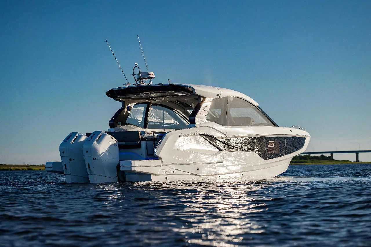A sleek white motorboat with dual engines floats on sparkling water under a clear blue sky, showcasing its modern design.