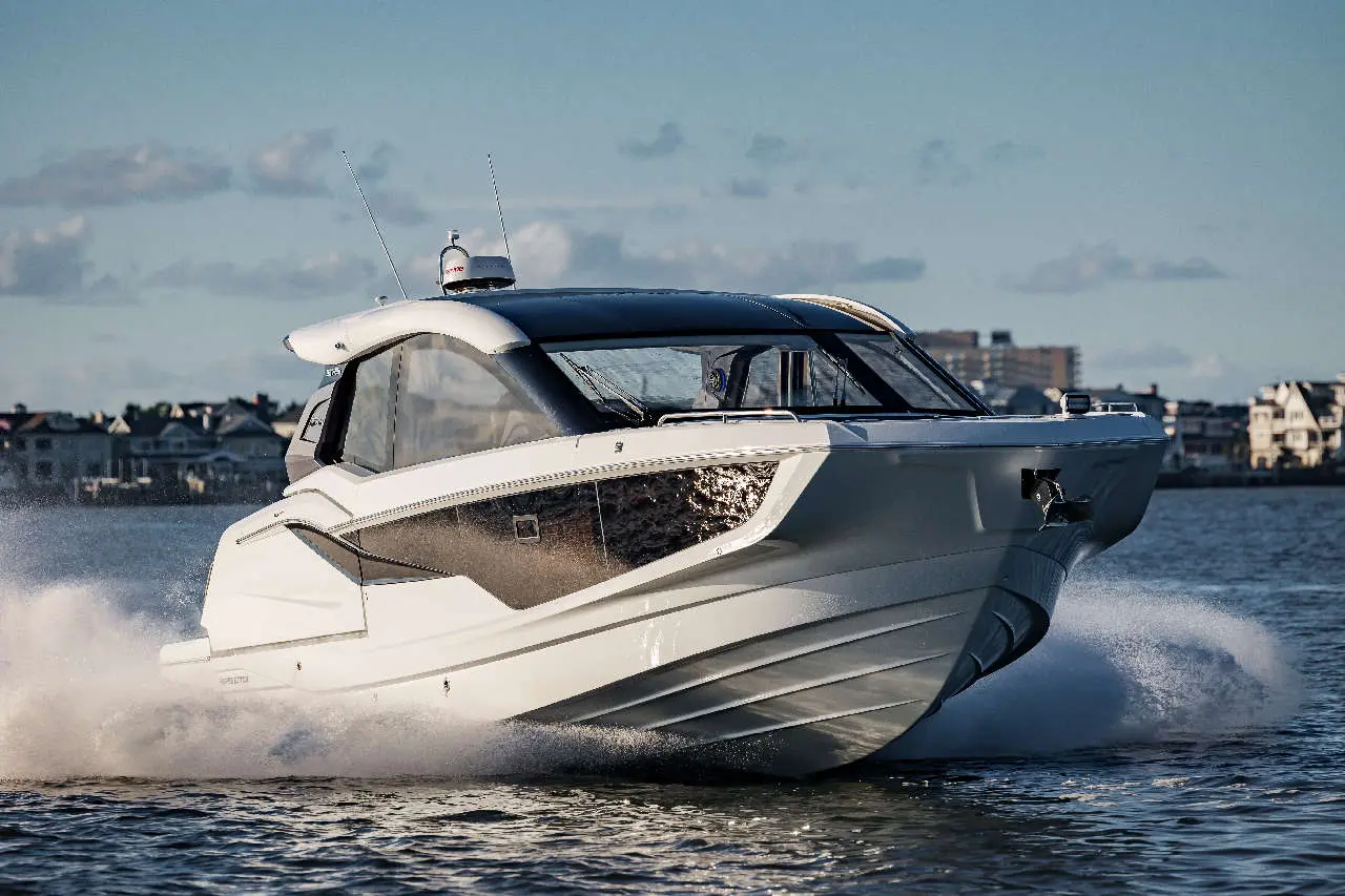 A sleek white motorboat splashes across the water with a coastal background, showcasing luxury and performance.