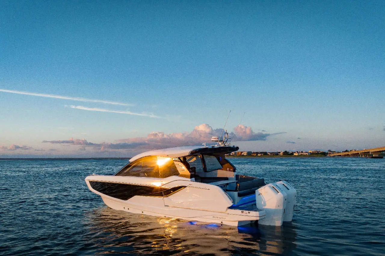 Luxury motorboat anchored on calm waters, reflecting sunlight, with a scenic evening sky and distant shoreline visible.
