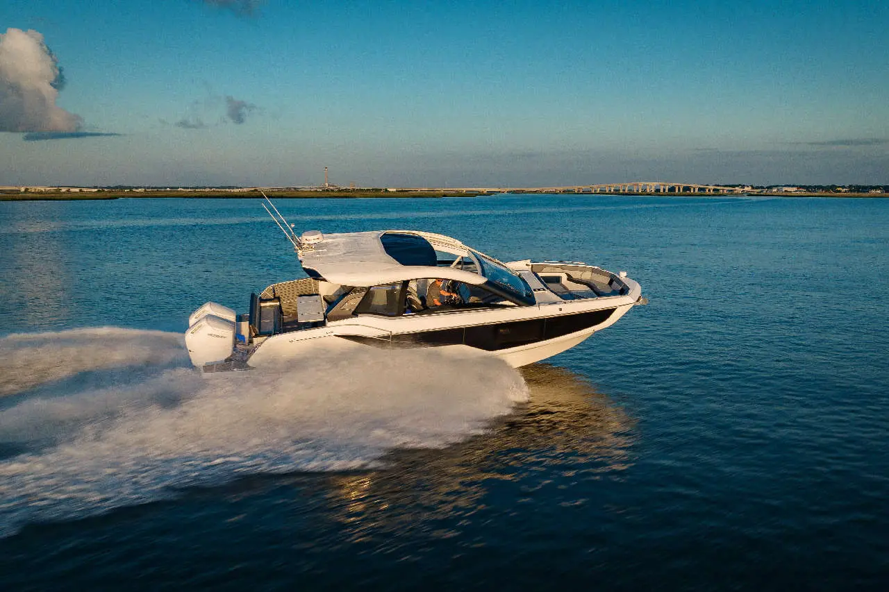 A sleek white powerboat accelerates across calm blue waters, leaving a trail of spray under a clear sky.