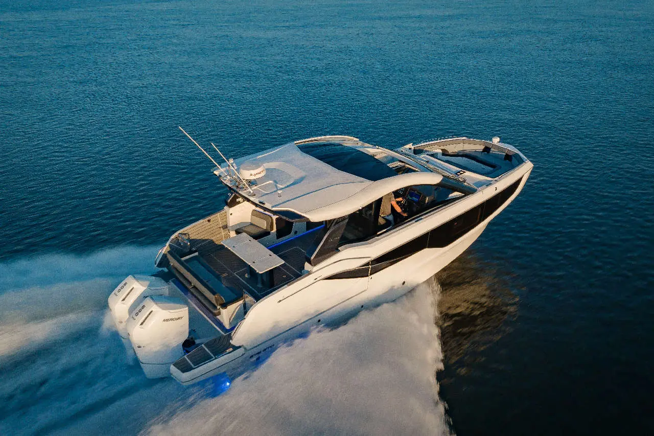 A sleek motorboat glides over water, powered by twin engines, with visible seating area and a captain at the helm.