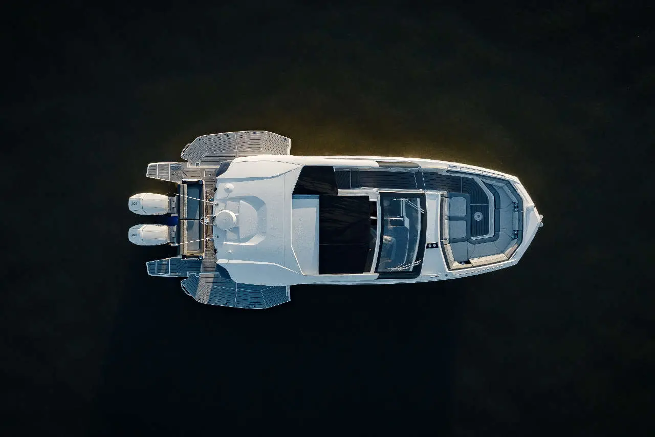Aerial view of a sleek white yacht with twin outboard motors, moored on dark water. Interior shows stylish seating and dashboard.