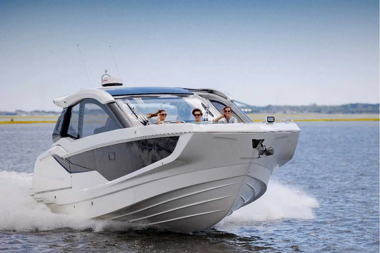 A sleek boat speeds across water with three passengers enjoying the ride on a sunny day.
