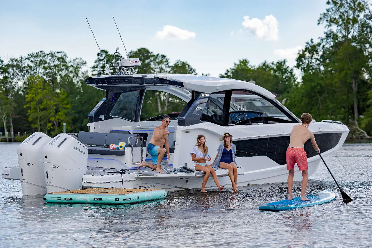 A group of four friends enjoying a gathering on a luxury boat, with one paddleboarding and others relaxing by the water.