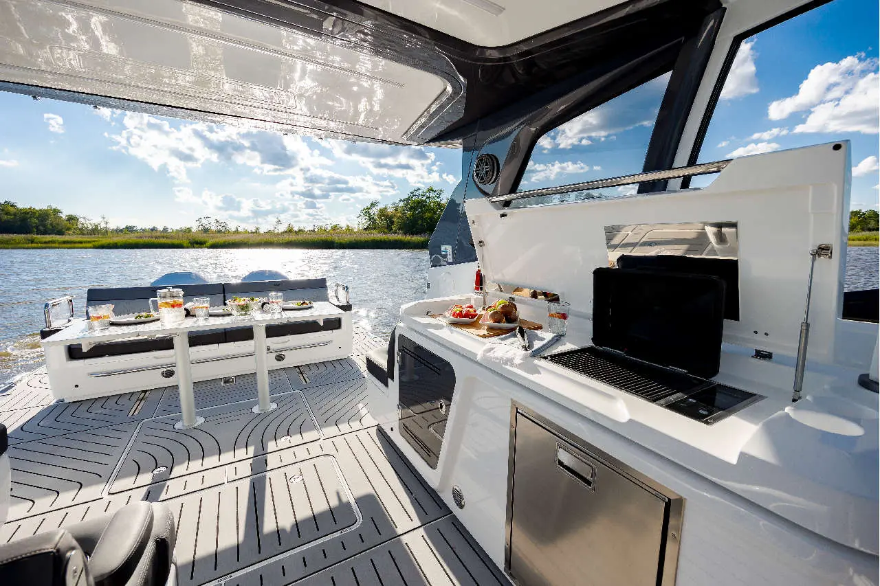 Modern boat interior featuring a dining area, outdoor views, and a compact kitchen with food and drinks prepared.