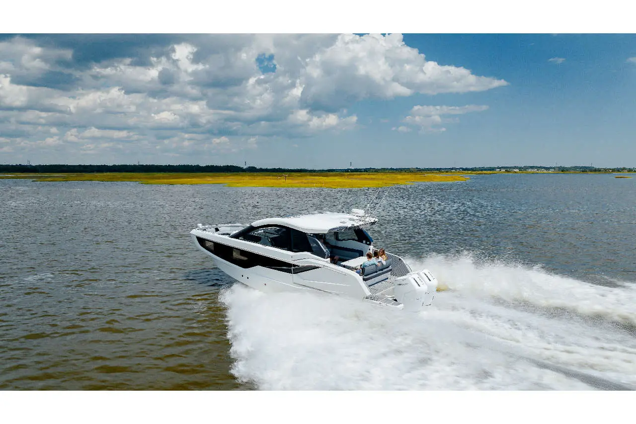 A sleek motorboat races across calm waters under a blue sky with clouds, showcasing a vibrant landscape in the background.