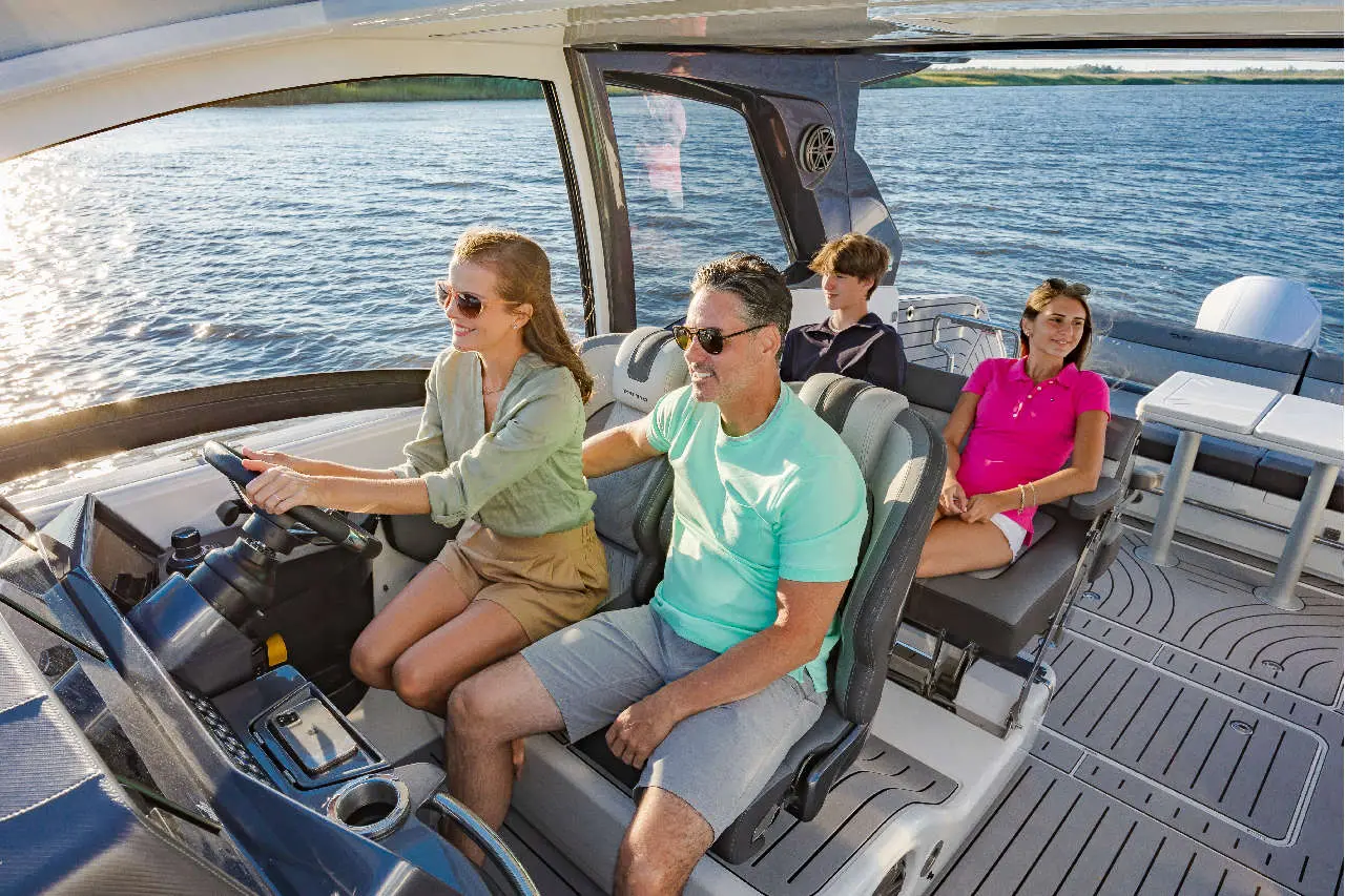 A woman steers a boat while three passengers, including a man and two children, enjoy a sunny day on the water.