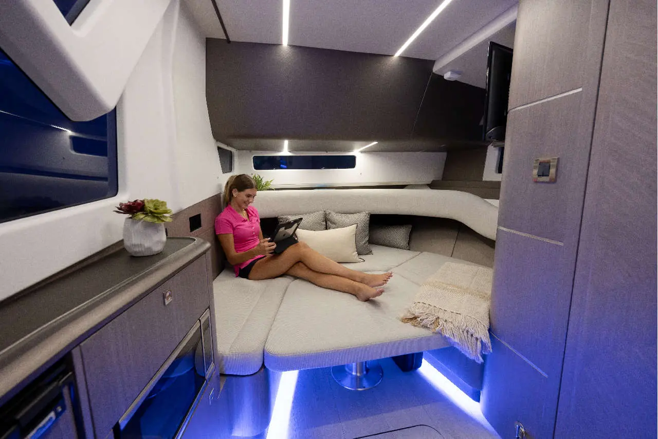 A woman in a pink top relaxes on a plush sofa in a stylish boat interior, using a tablet amidst modern furnishings.