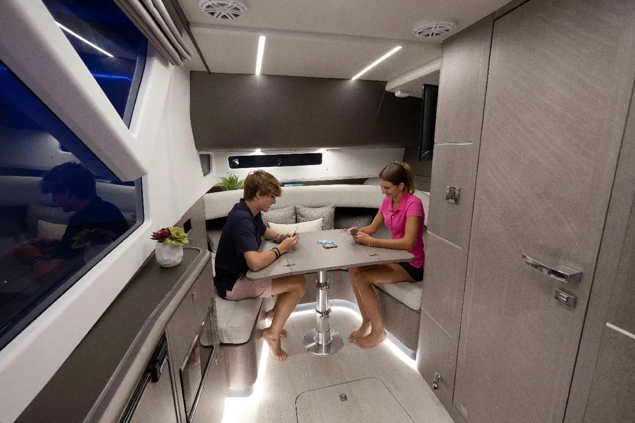 Two people seated at a modern table in a yacht interior, playing cards, with soft lighting and grey decor.