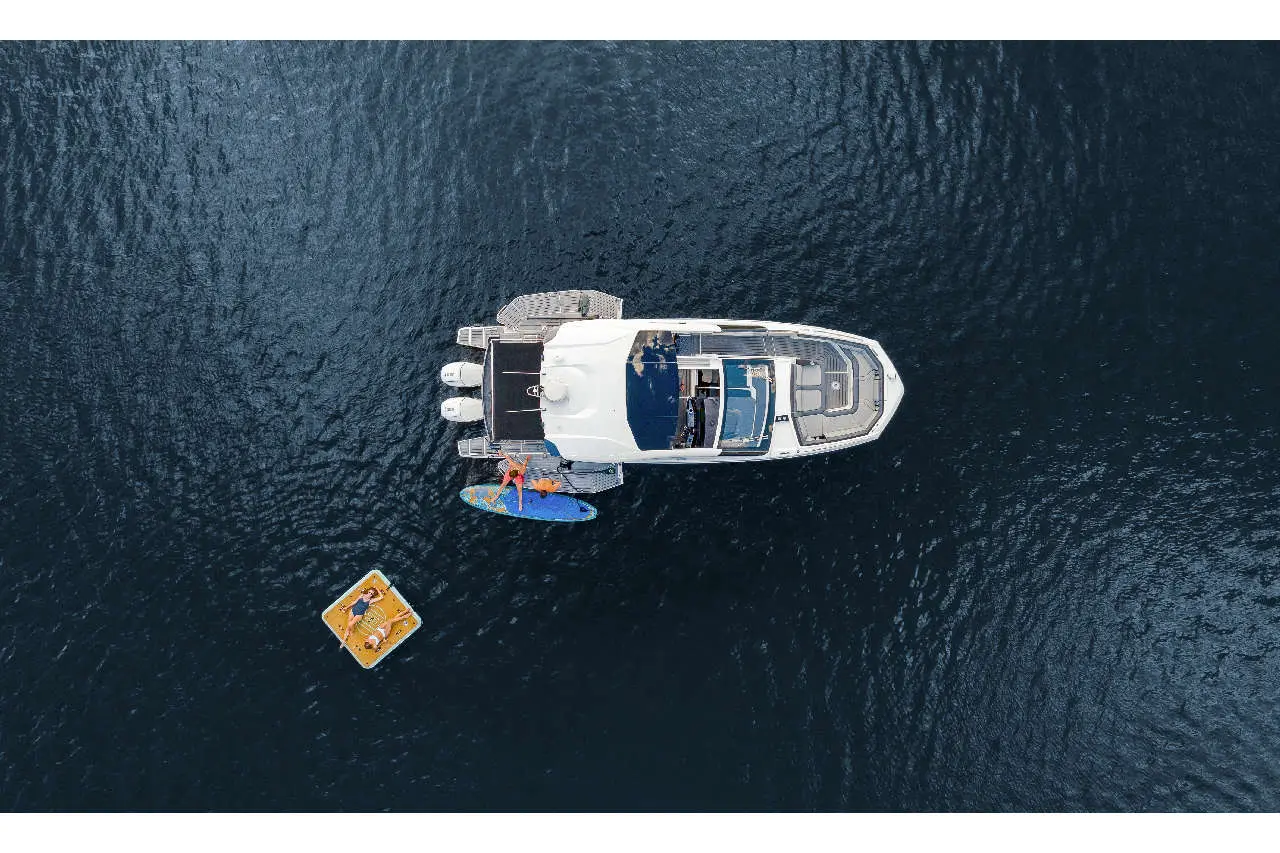 Aerial view of a white yacht with people on a paddleboard and a floating platform in deep blue water.
