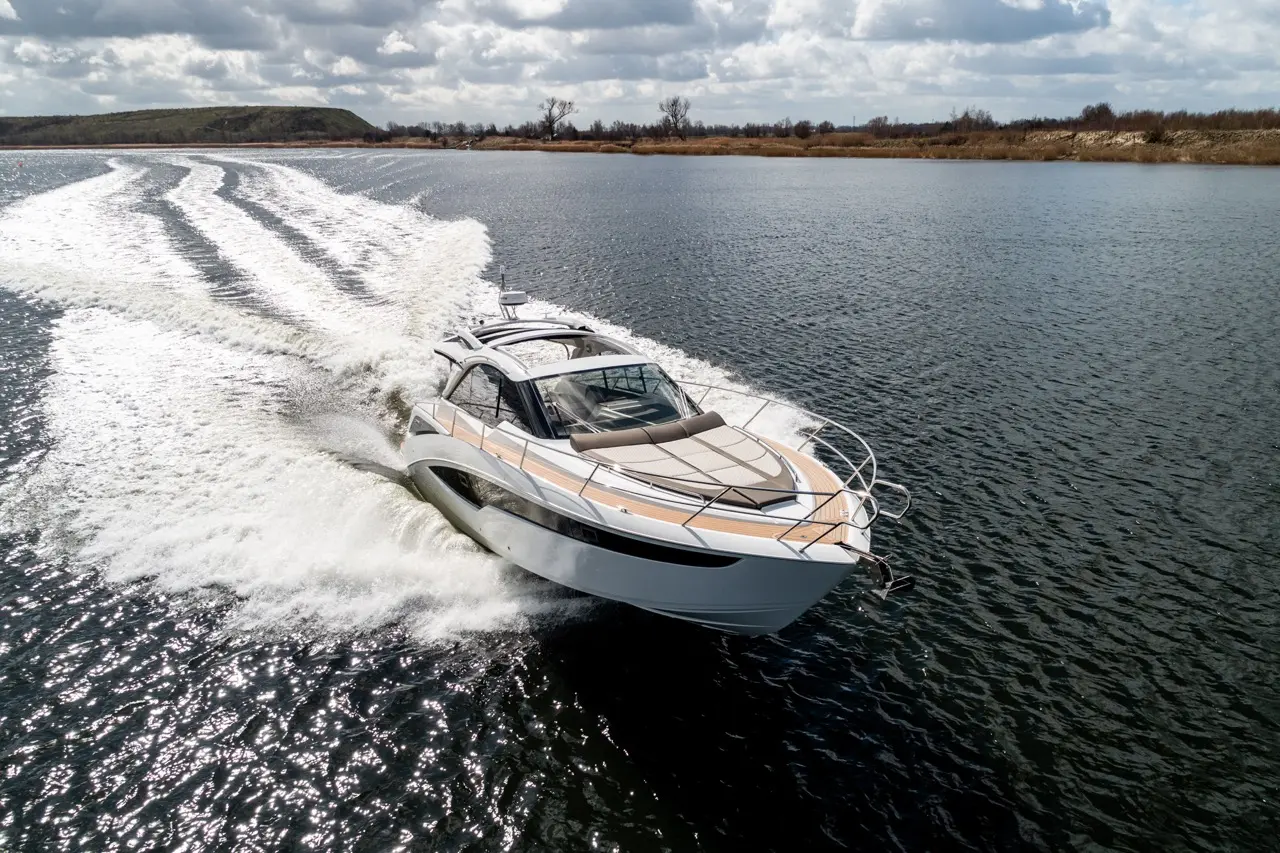 A sleek motor yacht glides through shimmering water, leaving a wake under a partly cloudy sky.