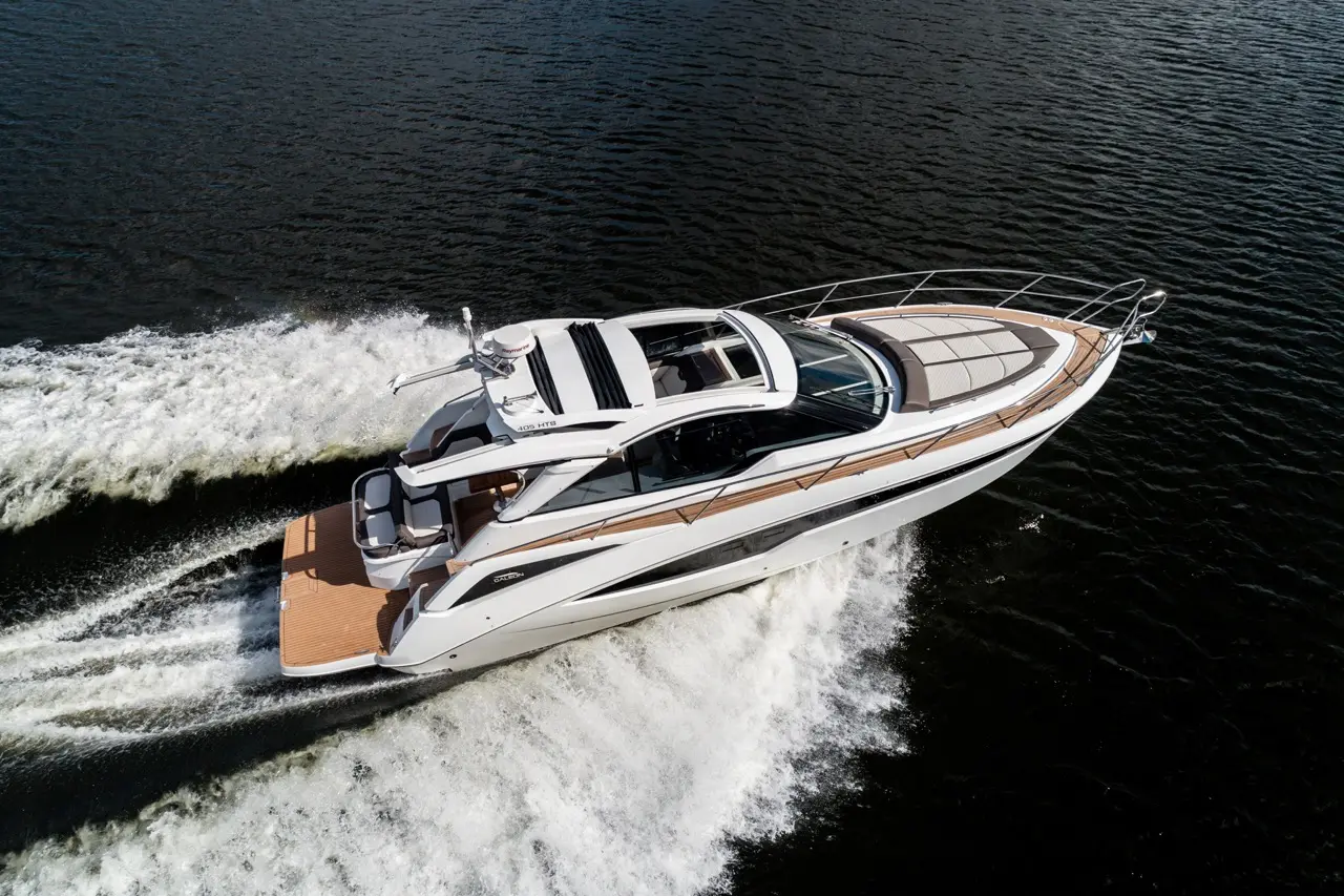 A sleek white motorboat cruises through water, creating a frothy wake against a dark backdrop, showcasing luxury and speed.
