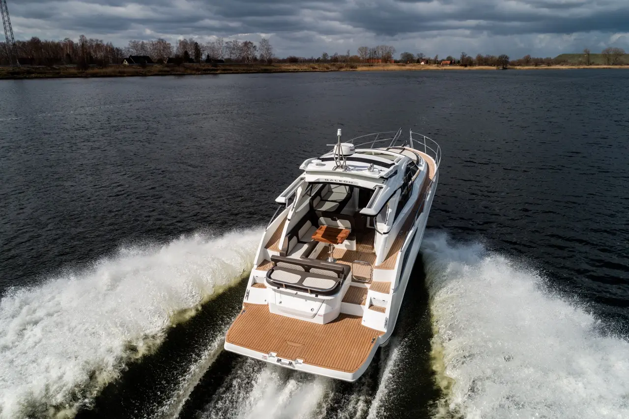 A sleek motorboat navigating a calm lake, leaving white wake trails against a backdrop of dark clouds and autumn trees.