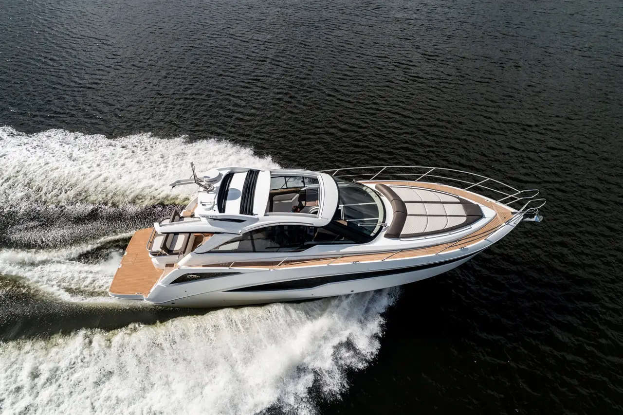 A sleek motor yacht glides through water, creating white spray, showcasing its elegant design and spacious deck.