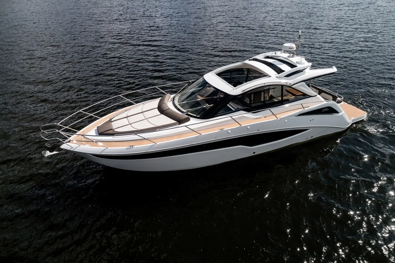 A sleek white motor yacht with a spacious deck glides over dark water under bright sunlight, showcasing modern design.