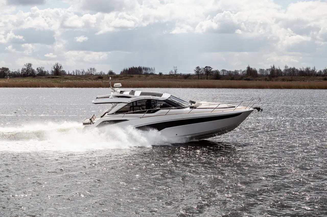 A sleek motorboat glides rapidly across a reflective lake with splashes of water, under a cloudy sky.