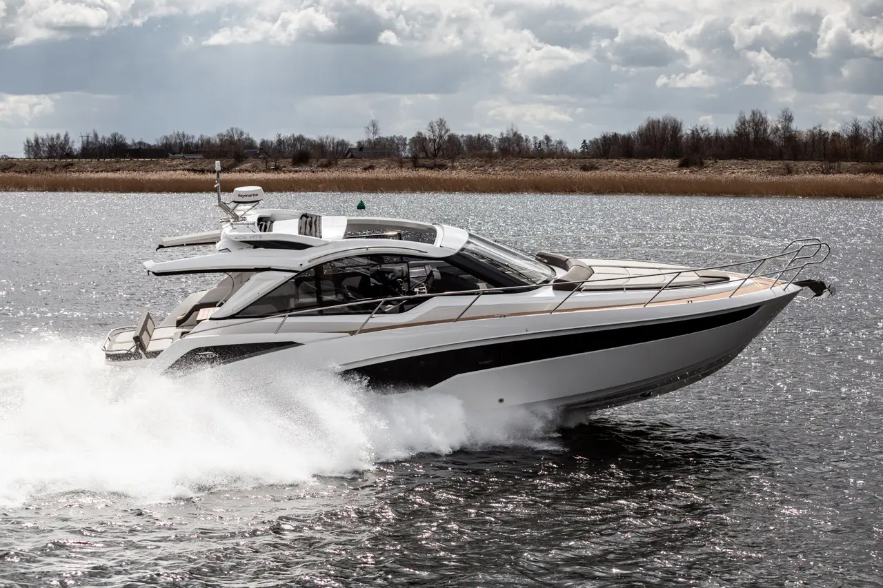A sleek white motorboat glides across shimmering water, creating a spray, under a partly cloudy sky.