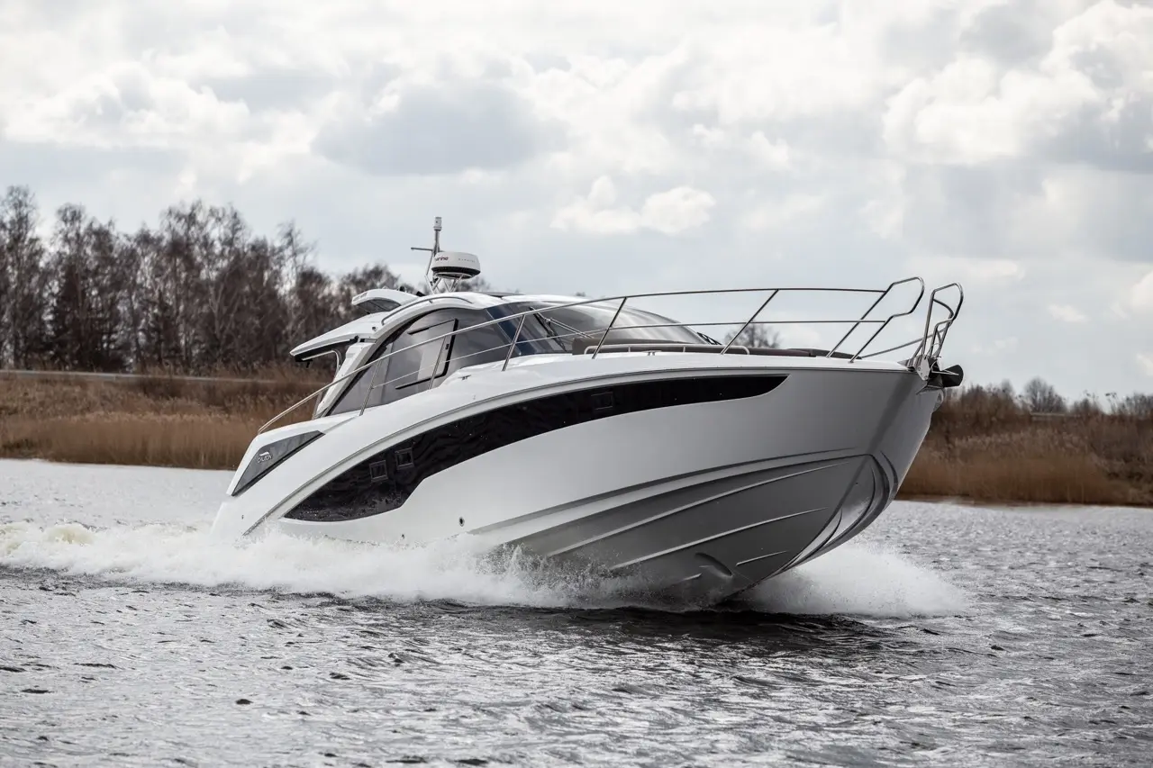 A sleek white motorboat speeds across a lake, leaving a spray of water in its wake under a cloudy sky.