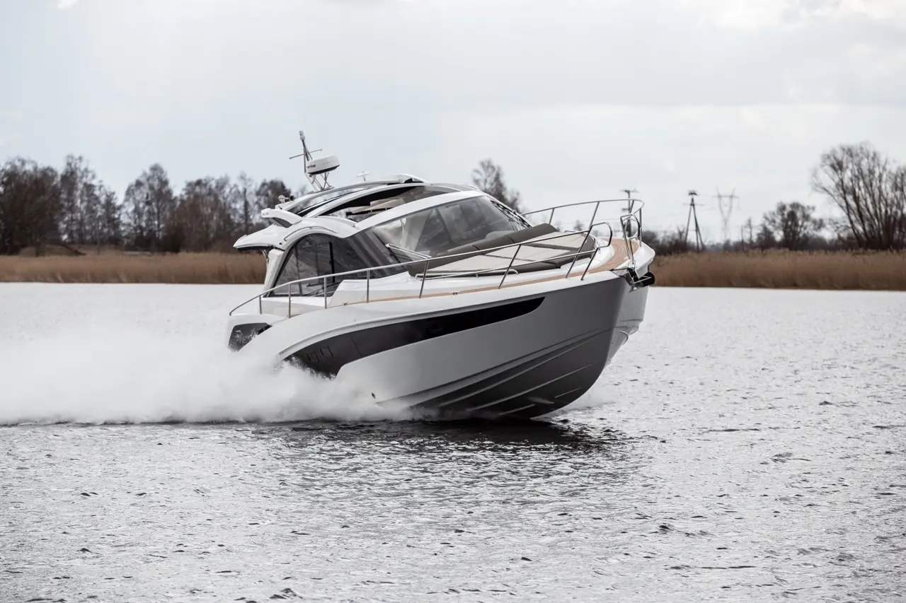 A sleek motorboat skimming across a lake, sending up spray, surrounded by clouds and trees in the background.