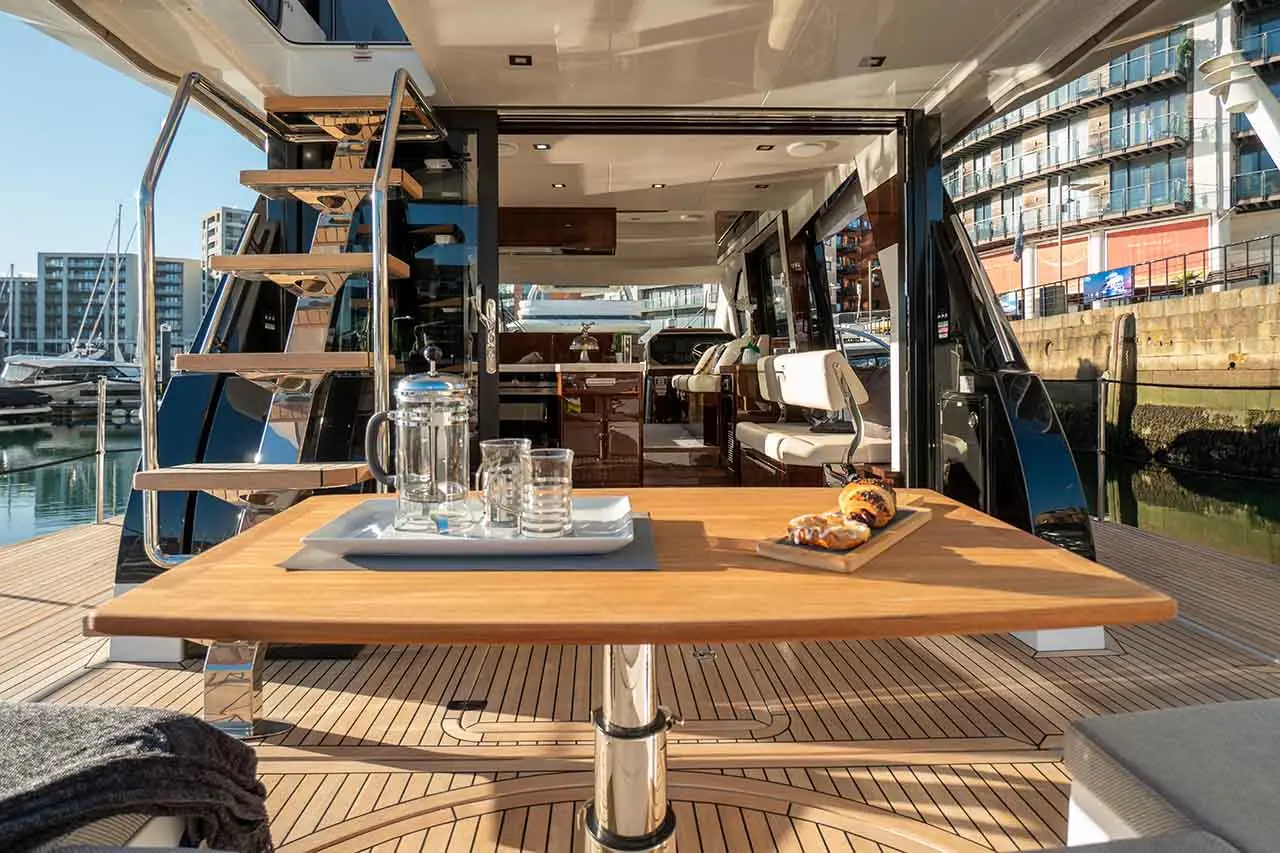 Luxurious yacht interior featuring a wooden table with refreshments, a scenic view of the marina, and stylish seating area.
