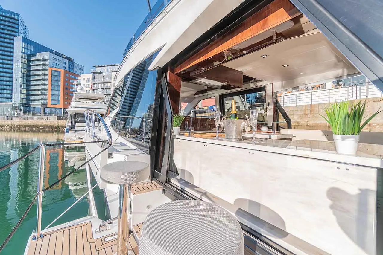 Luxury yacht with a modern bar area, overlooking water and city high-rises, featuring champagne and stylish seating.