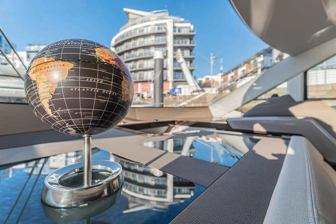 A globe highlighting South America rests on a reflective surface, with contemporary buildings and clear blue sky in the background.