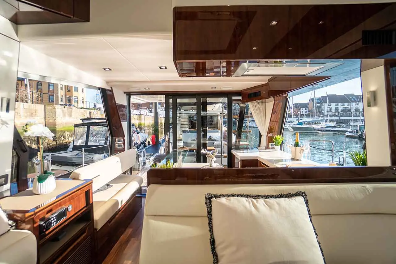 Luxurious yacht interior with cream seating, modern decor, and large windows showcasing the marina and parked boats outside.