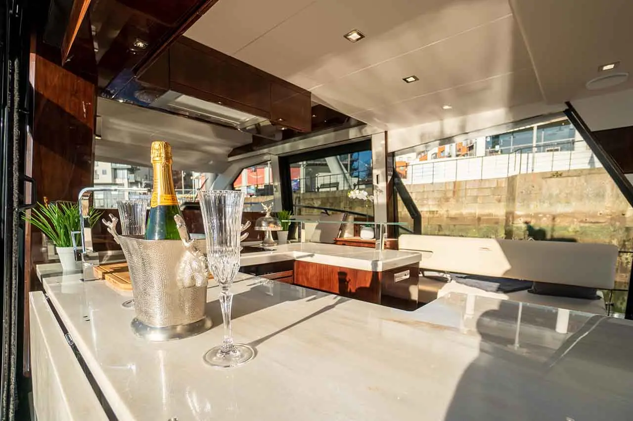 Luxury yacht bar with champagne, crystal glasses, and a modern design. Sunlight illuminates a stylish interior with greenery.