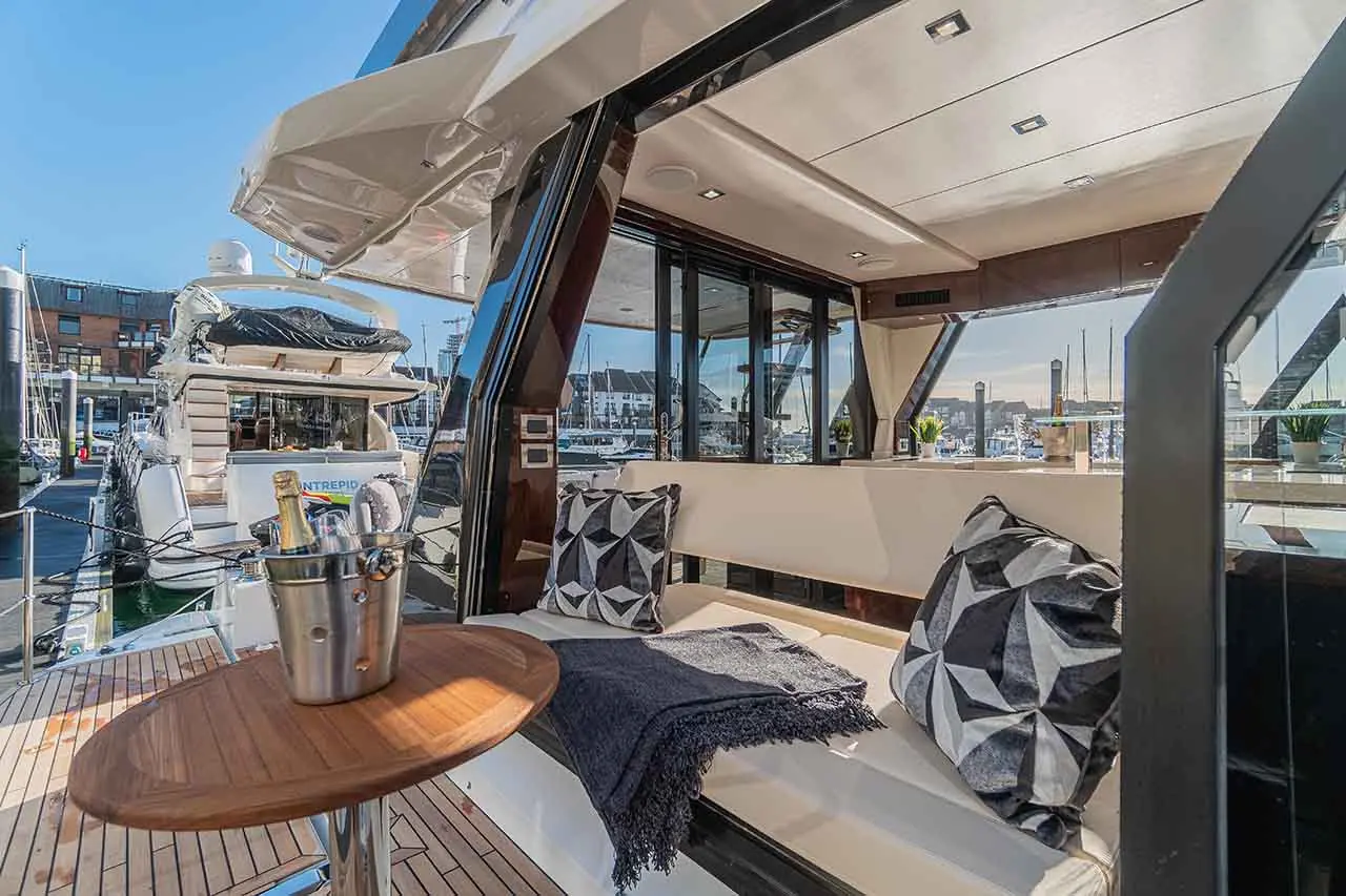 Luxurious yacht interior featuring seating area, patterned cushions, a small table with a champagne bucket, and marina views.