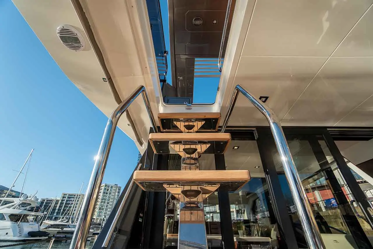 View of sleek yacht stairs leading to an upper deck, with clear blue sky and marina buildings in the background.