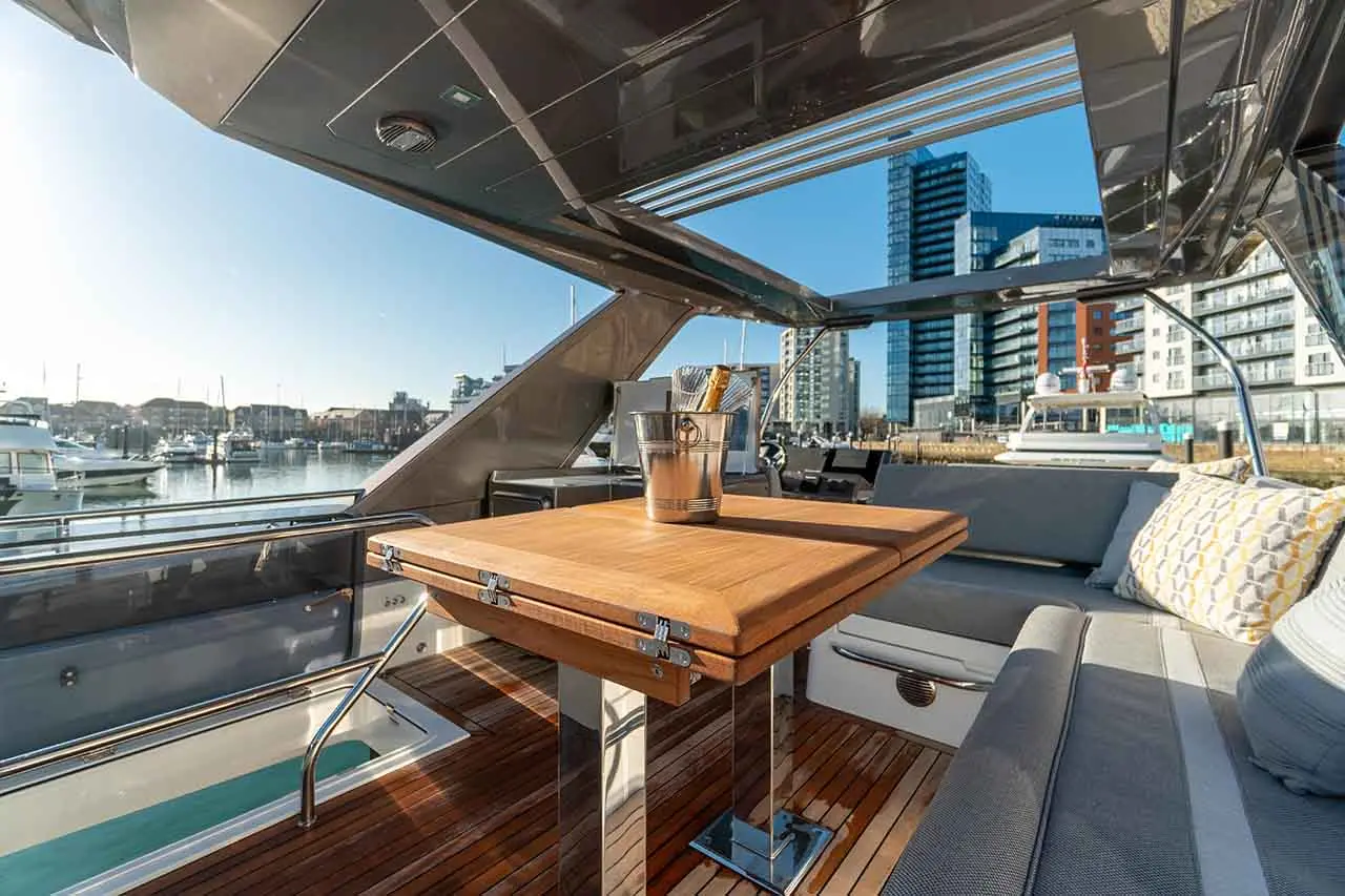 Luxurious yacht deck featuring a wooden table, drinks bucket, and city skyline view with nearby boats and modern buildings.