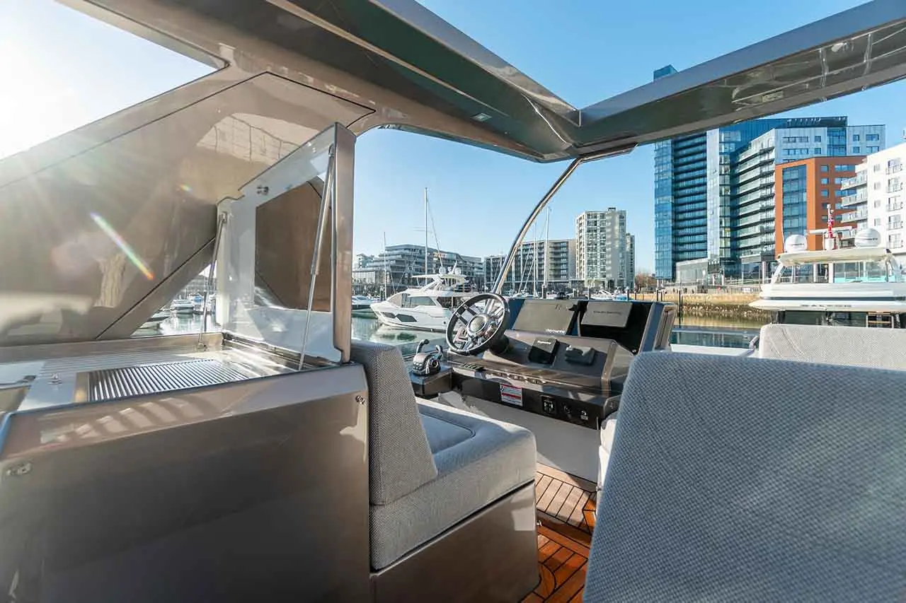 Interior view of a modern boat cockpit showcasing a steering wheel, seating, and marina landscape with buildings.