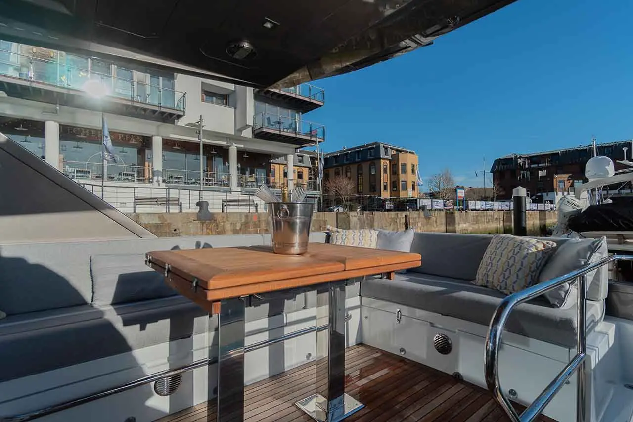 Chic boat seating area featuring a wooden table, silver ice bucket, and views of waterfront buildings under a bright blue sky.