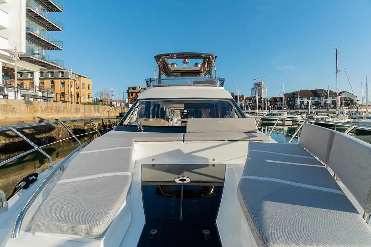 Luxury yacht at a marina, featuring sleek design, sunbeds, and nearby modern waterfront buildings under a clear blue sky.