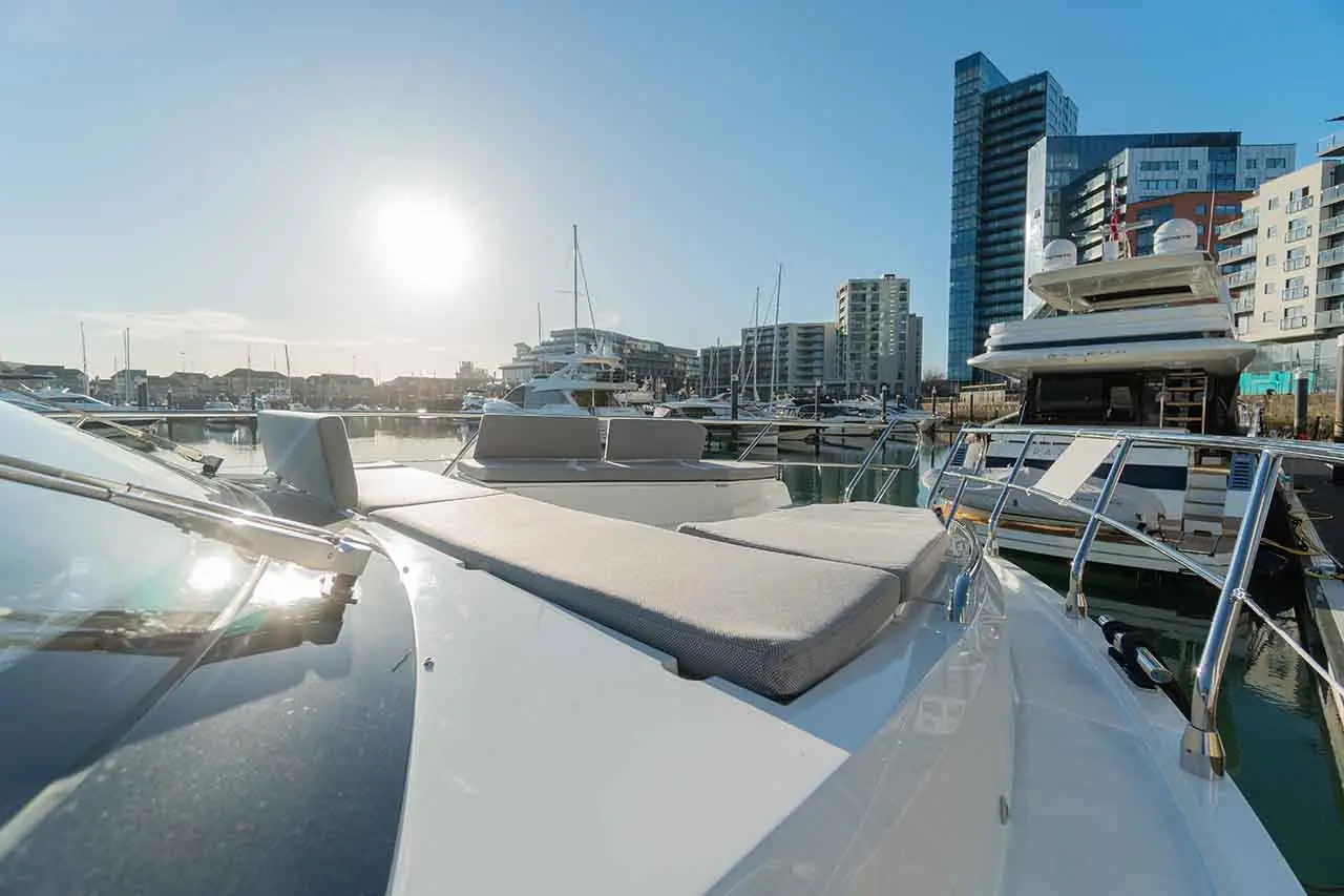 View of a marina with yachts and modern buildings under a bright sky, sun reflecting on the boat's deck.