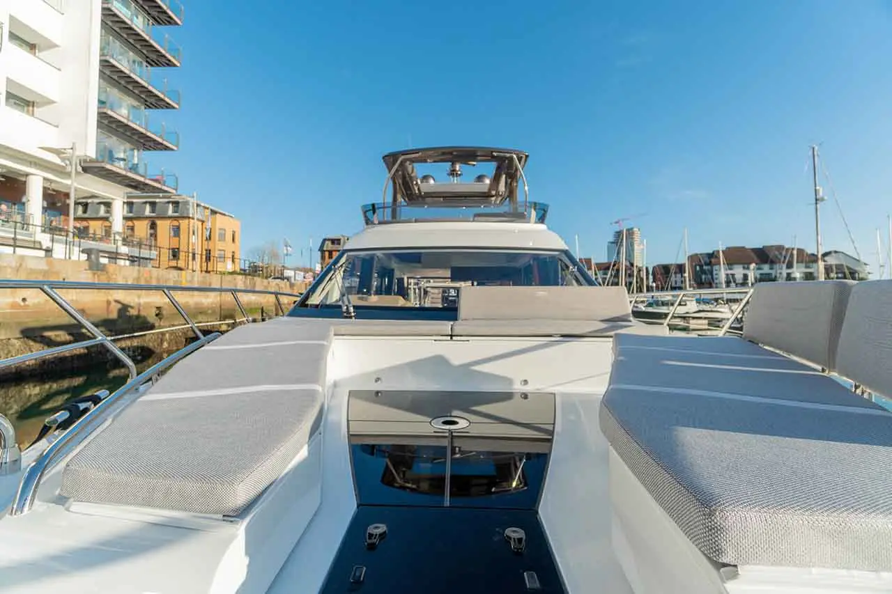 Luxury boat view from the bow, highlighting cushioned seating and buildings along the marina under a clear blue sky.