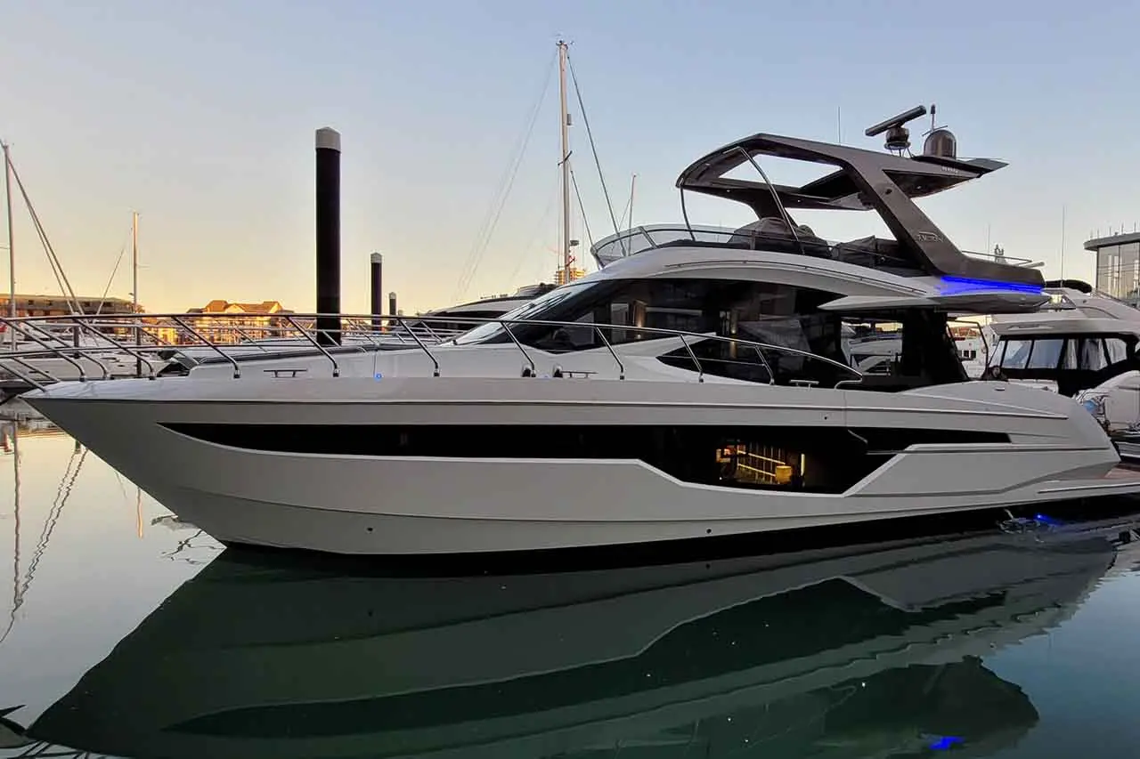 Luxury motor yacht docked at sunset, reflecting in calm water, highlighting sleek design and spacious exterior features.