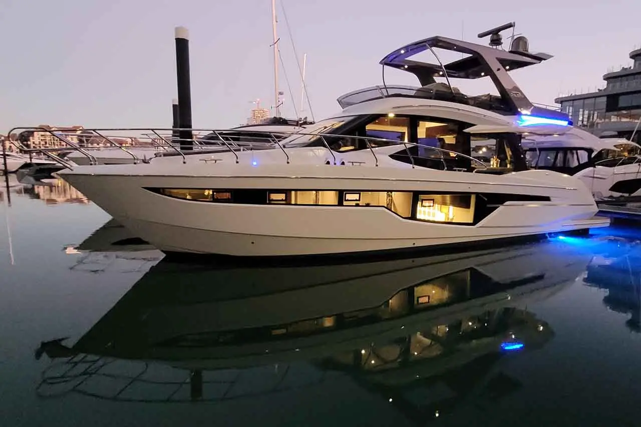 Luxury motor yacht at sunset, showcasing sleek design, illuminated interior, and reflections in calm marina waters.