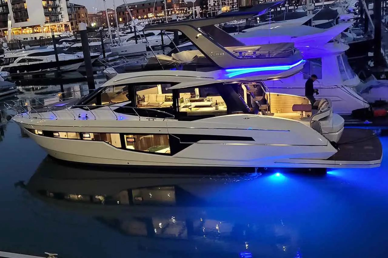 Luxurious yacht docked at night with blue lights illuminating the water, surrounded by other boats in the marina.