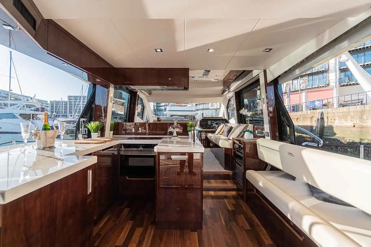 Luxury yacht interior featuring a modern kitchen, lounge area, and large windows offering marina views.