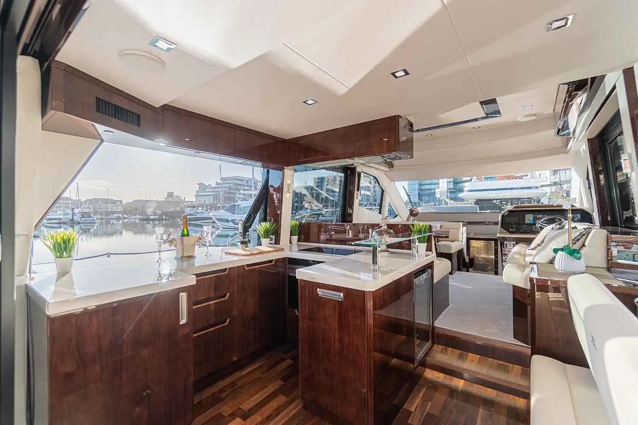 Modern yacht interior featuring a sleek kitchen, seating area, and views of the marina and boats outside.