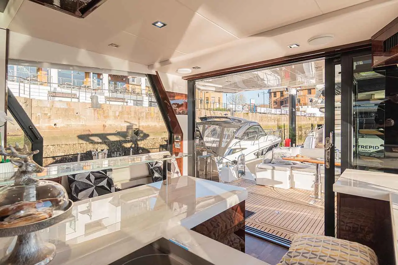 Interior view of a luxurious boat with a view of the dock, featuring modern furnishings and a sleek yacht outside.